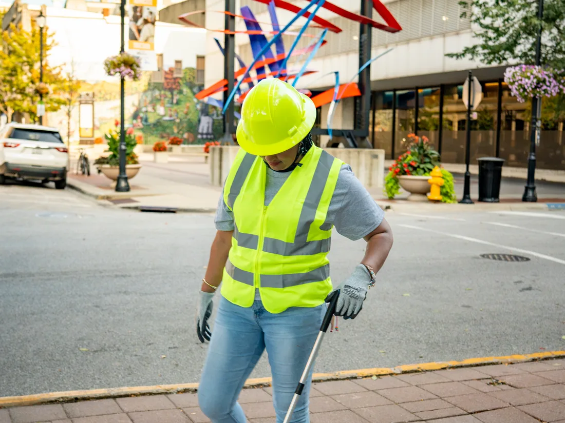 A Star City Environmental crew member crossing a commercial street with a litter grabber.