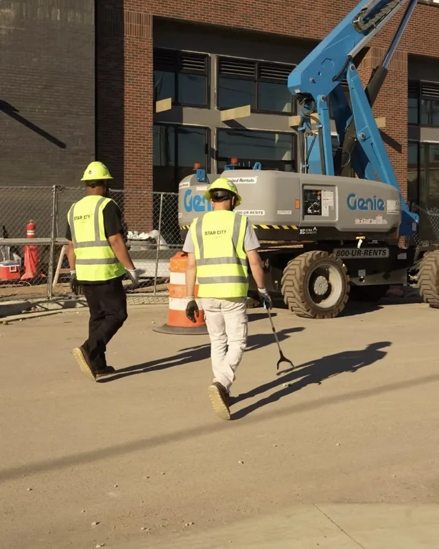 Star City Environmental crew members carrying litter grabbers across a job site cleanup in Lafayette, Indiana.