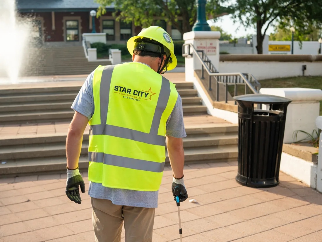 A Star City Environmental crew member in a branded high-visibility vest working a receptacle round downtown.