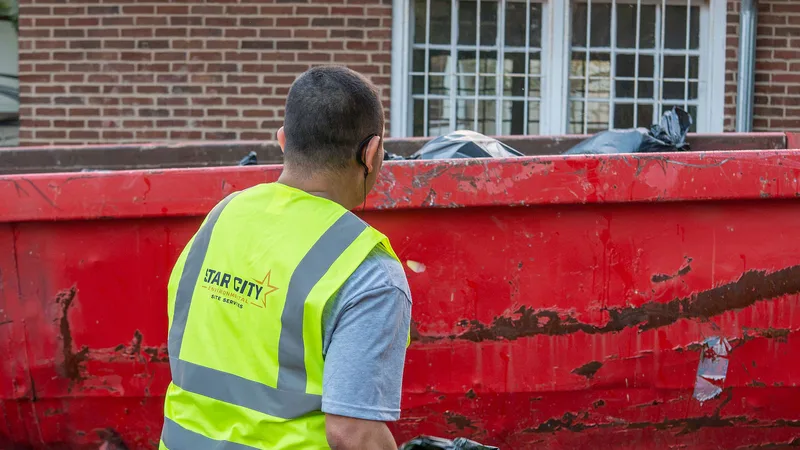 A Star City Environmental crew member loading collected waste into a dumpster at a residential property.