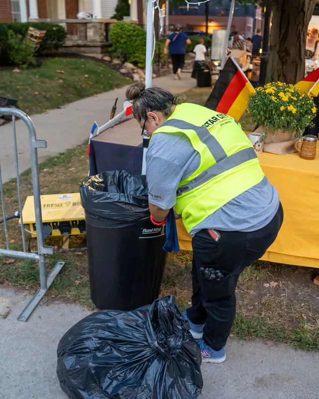 A crew member bagging waste beside a festival stall.
